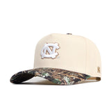 The No Rivals UNC Camo Connector Hat features a beige cotton build, white embroidered NC logo on the front, camo-patterned brim, structured fit, snapback closure, and a small embroidered N on the side.