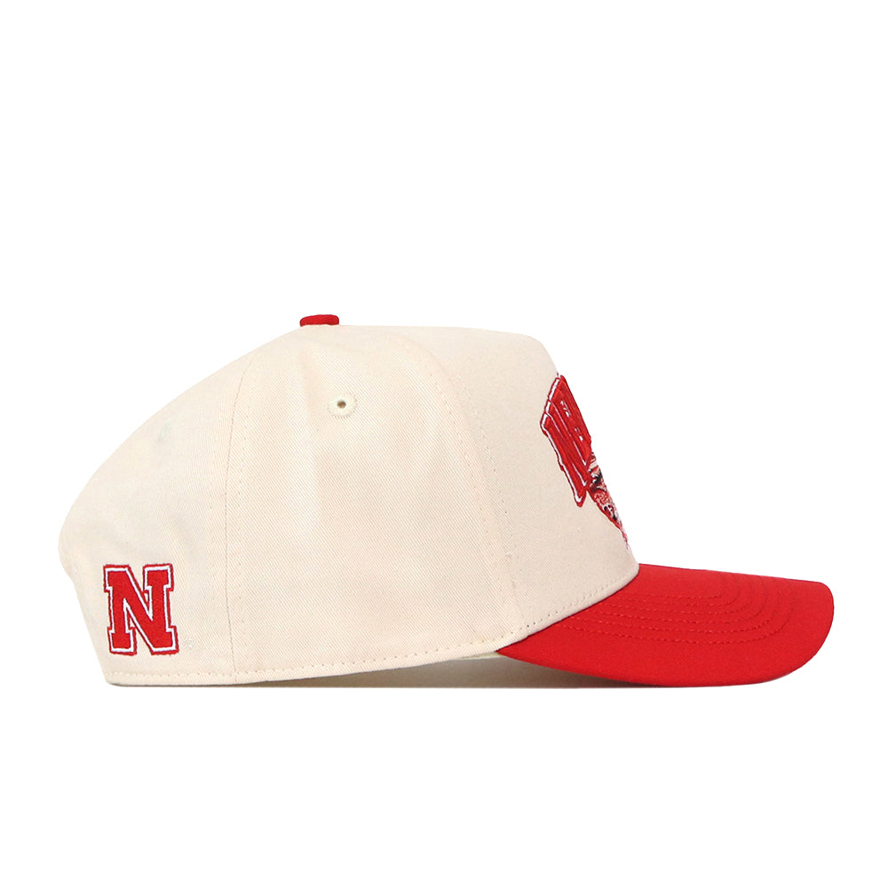 Here’s a rewritten version using your product data: The Nebraska Cornhuskers Stadium Hat by No Rivals is a cream and red snapback featuring a bold red “N” embroidered on the side and a matching red brim. Crafted mainly from cream fabric, this cap showcases detailed embroidered logos and is presented here in a side profile view.