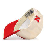 A Nebraska Cornhuskers Stadium Hat by No Rivals is shown upside down, featuring a bold red embroidered N logo, a red brim, and an officially licensed inside tag with the phrase “NO RIVALS” and a QR code.