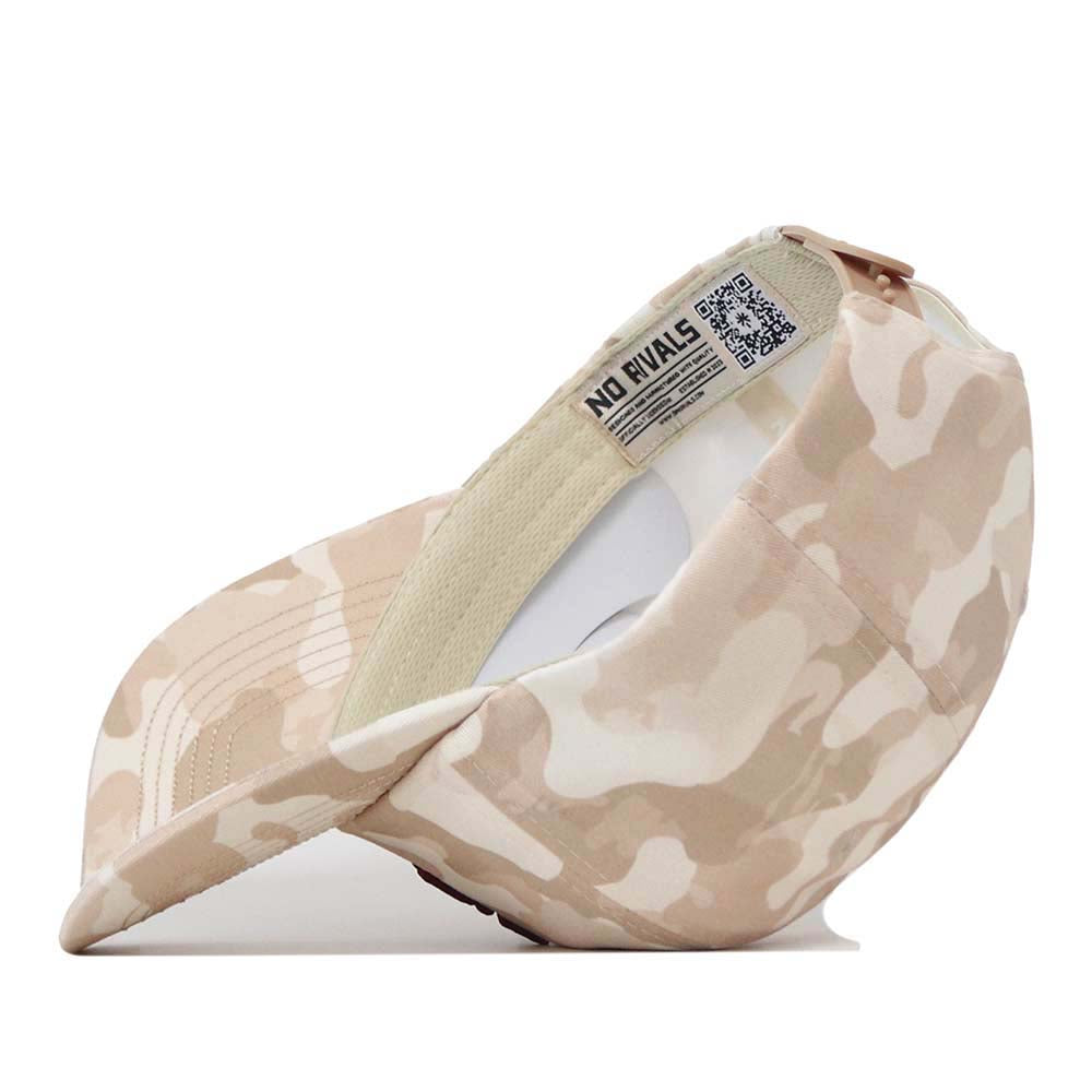 A side view of the Texas A&M Sand Camo Hat - Unstructured by No Rivals is shown, highlighting its beige and cream camouflage pattern, curved brim, adjustable strap, and inside label featuring the No Rivals branding and a QR code.