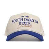 The No Rivals South Dakota State Vintage Hat is a white cap with a blue brim, featuring “EST 1881 SOUTH DAKOTA STATE Jackrabbits” embroidered on the front. This officially licensed snapback also displays a detailed embroidered logo for added style and authenticity.