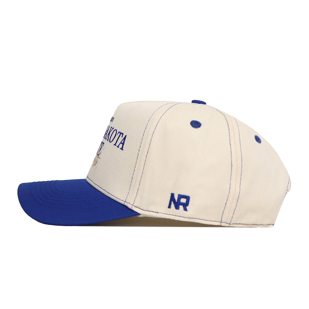 Introducing the South Dakota State Vintage Hat by No Rivals—a beige baseball cap featuring a blue brim and blue stitching. The initials “NR” are embroidered on the side, alongside an officially licensed embroidered South Dakota State logo. Its adjustable snapback design ensures a comfortable fit for all.