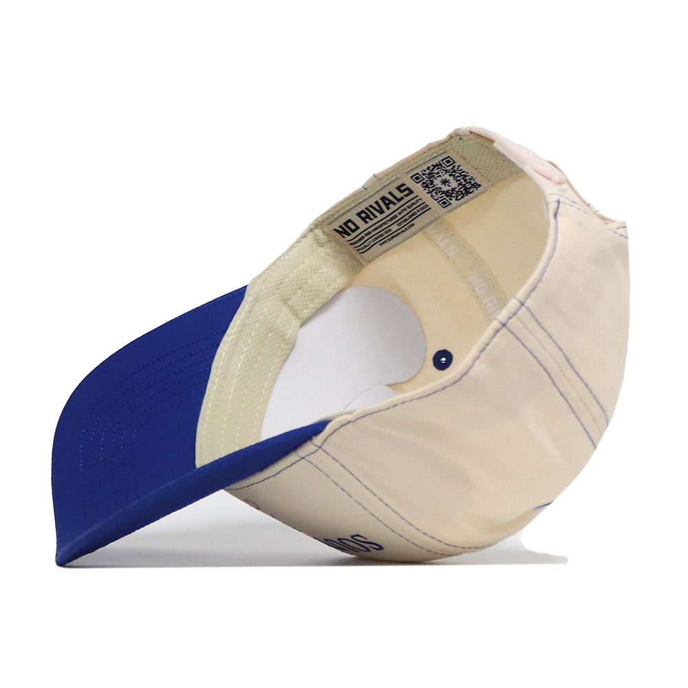 A South Dakota State Vintage Hat by No Rivals is displayed upside down, showcasing the inner labels, stitching, and adjustable snap back strap. This officially licensed beige and blue cap features an embroidered logo for added detail.