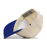 A South Dakota State Vintage Hat by No Rivals is displayed upside down, showcasing the inner labels, stitching, and adjustable snap back strap. This officially licensed beige and blue cap features an embroidered logo for added detail.