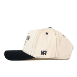 Side view of a beige Kennesaw State Owls Vintage Hat by No Rivals, featuring a black snapback brim, black stitching and eyelets, and an embroidered NR logo in black on the side.