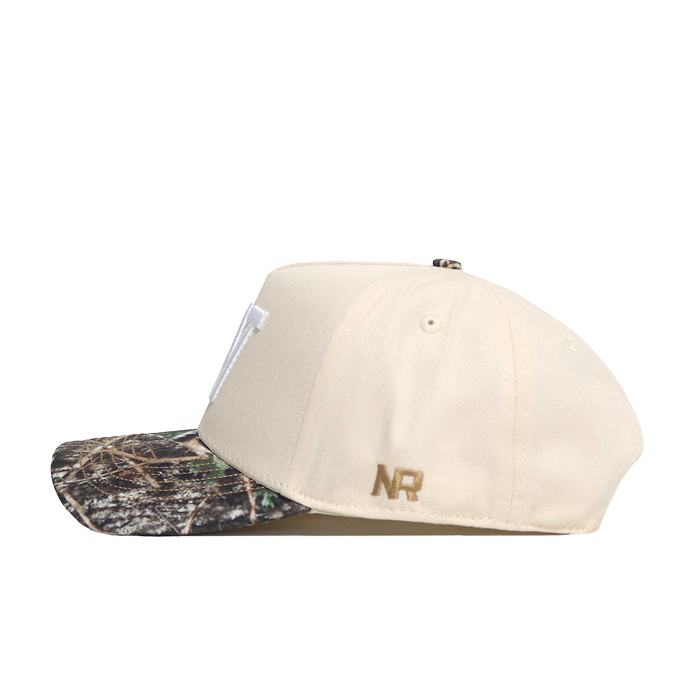 The Washington Camo Connector Hat by No Rivals is a beige snapback featuring a camouflage-patterned brim and gold "NR" embroidery on the side. The cap showcases embroidered logos and is displayed from a side angle against a white background.