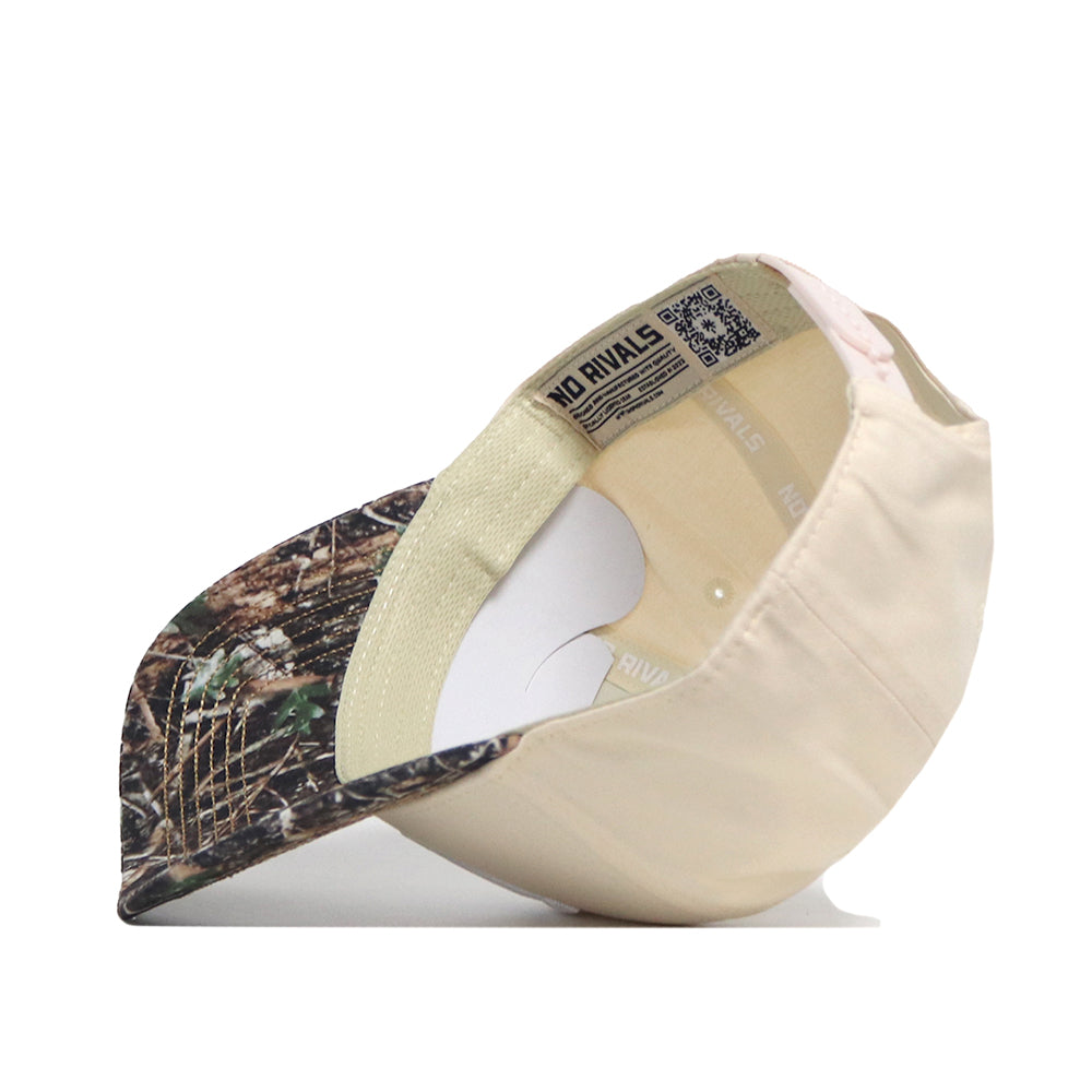 The Washington Camo Connector Hat by No Rivals is flipped over to display its interior lining, tags, and an inner label reading NO RIVALS. The hat features a beige snapback design with a camouflage-patterned brim.