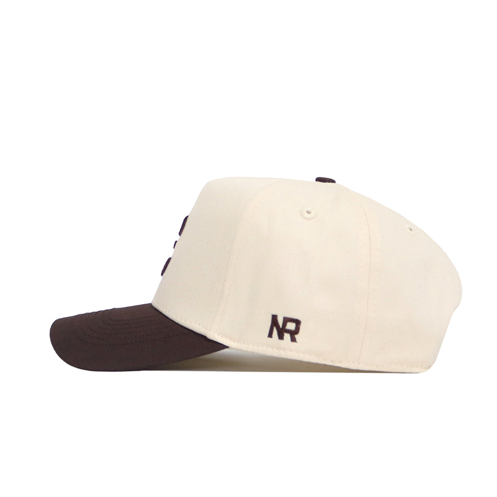 The No Rivals ETSU Espresso Hat is a cream snapback with a dark brown brim, made from high-quality cotton. It features “NR” embroidered in brown on the side, shown against a plain white background.