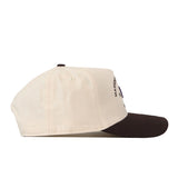 Side view of the No Rivals Washington Huskies Outlaw Hat – Classic, featuring a beige crown with a black brim, two ventilation eyelets, and a partially visible officially licensed embroidered Washington Huskies logo on the front.