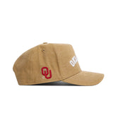 The Oklahoma Rustic Hat by No Rivals is a tan cotton canvas hat featuring "OKLAHOMA" embroidered in white on the front and a red OU logo on the side, shown here in a structured fit from a side profile against a white background.