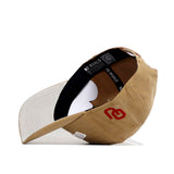 The Oklahoma Rustic Hat by No Rivals, in tan cotton canvas, is shown upside down to reveal its black inner lining, white underside brim, and interior band featuring “NO RIVALES” text and a red embroidered logo. Snap back style.