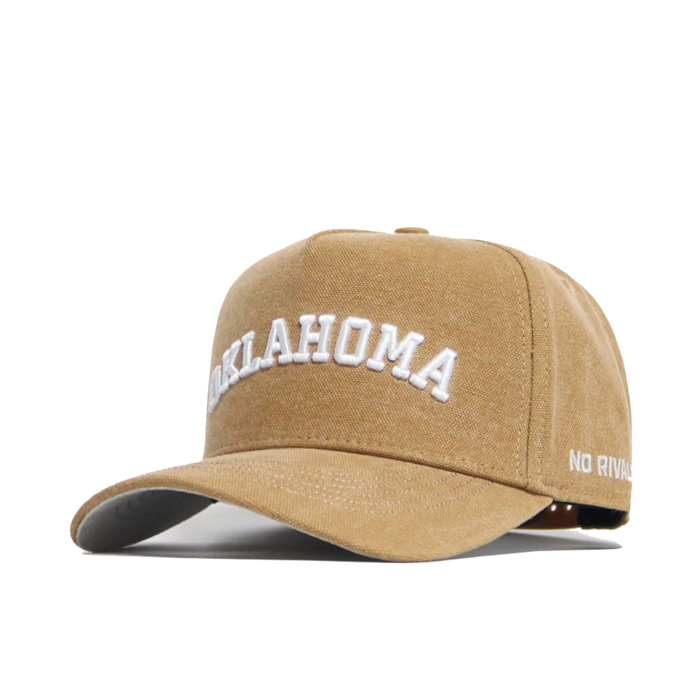 The Oklahoma Rustic Hat by No Rivals is a tan cotton canvas hat with "OKLAHOMA" embroidered in white on the front, "NO RIVALS" on the side, a structured fit, curved brim, and adjustable snap back for comfort.