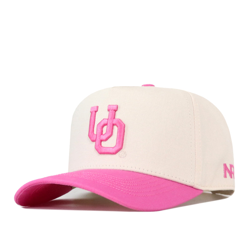 Show your support for the Breast Cancer Foundation with the Oregon Pink Out Hat by No Rivals. This officially licensed white snapback features a vibrant pink brim and bold pink embroidered “UD” letters on the front, accented with smaller pink text on the side for a stylish look.