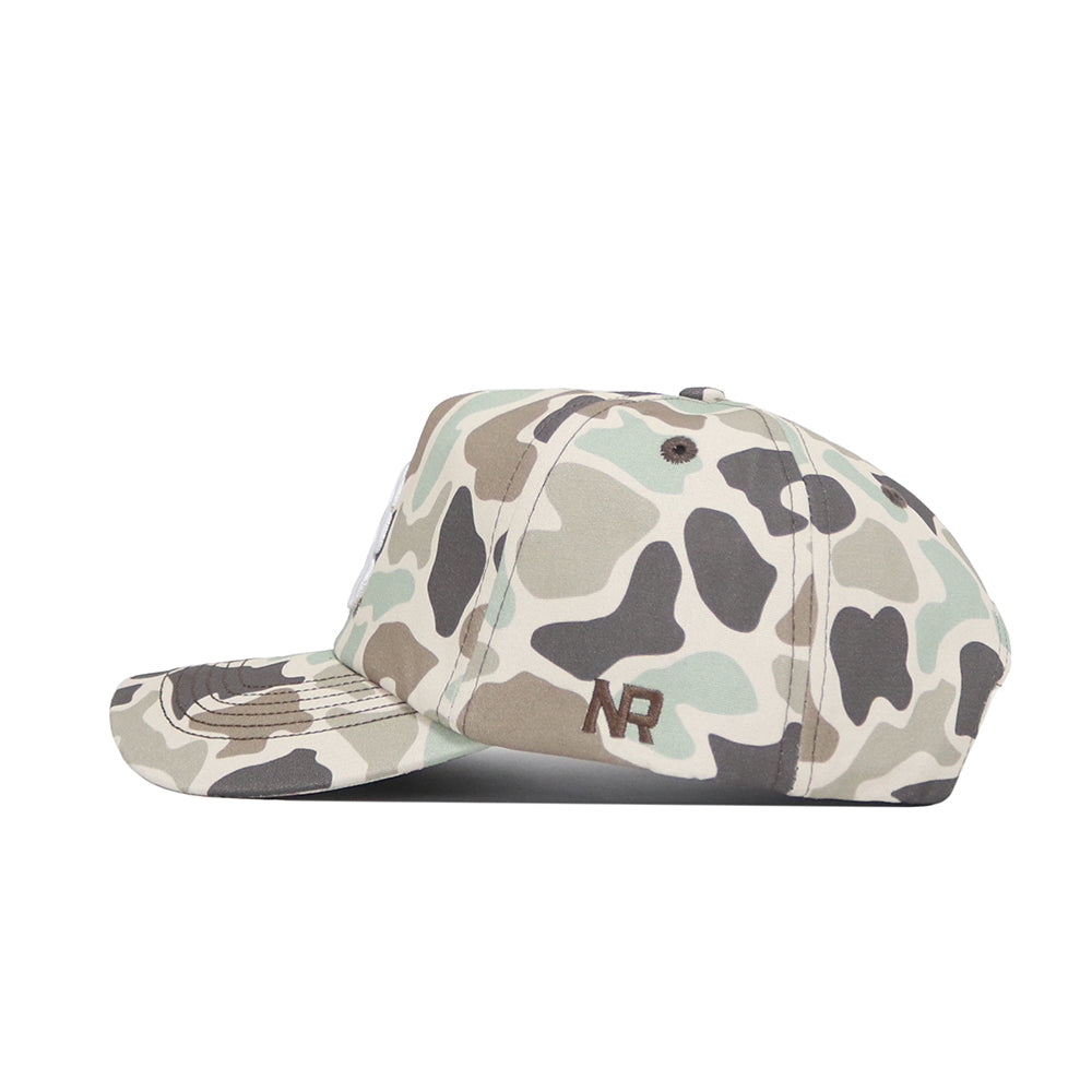 A side view of the Montana Huntsman Hat by No Rivals, a 5-panel cap in green, brown, and beige duck camo with "NR" embroidered in dark brown thread on the side.