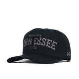 The Tennessee Night Mode Hat by No Rivals is a black cotton baseball cap with a flat brim, featuring “TENNESSEE” in large raised gray letters and an emphasized T on the front, plus NR embroidery on the side. Structured fit.