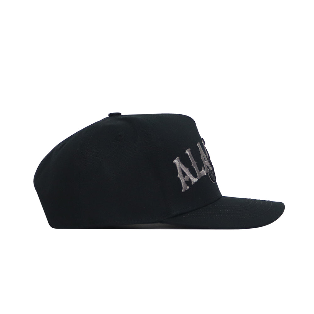 The Alabama Night Mode Hat by No Rivals is a black snapback crafted from premium cotton, featuring partially visible white embroidered lettering on the front panel, displayed from the left side against a white background.