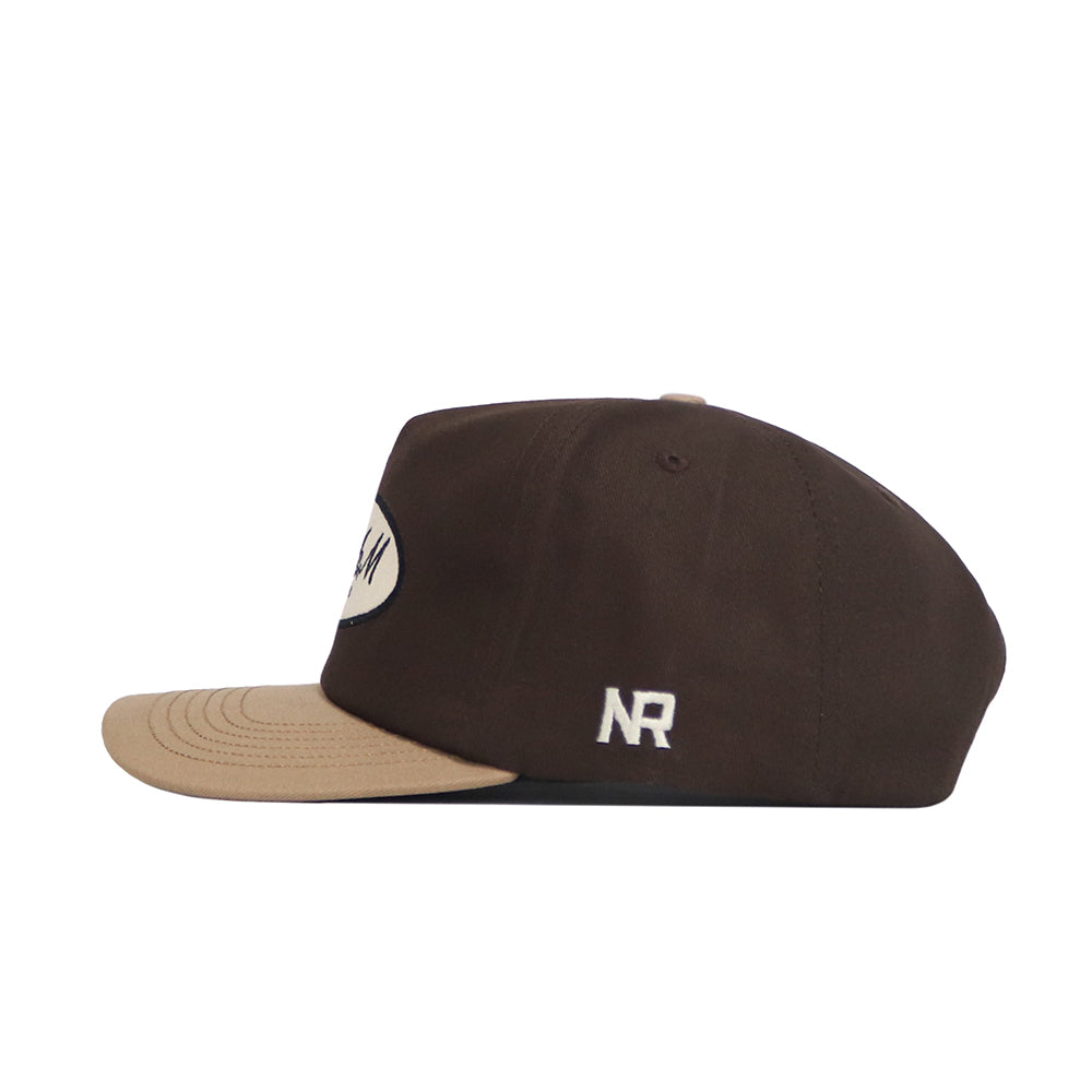 The Texas A&M Neutral Patch Hat by No Rivals is a brown snapback with a beige brim, a front embroidered white oval patch, and "NR" in white on the side for a structured fit.