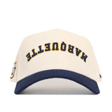 The Upside Down MARQUETTE Hat by No Rivals is a white cotton-canvas snapback with a navy blue brim, featuring "MARQUETTE" embroidered in yellow and navy blue across the front.