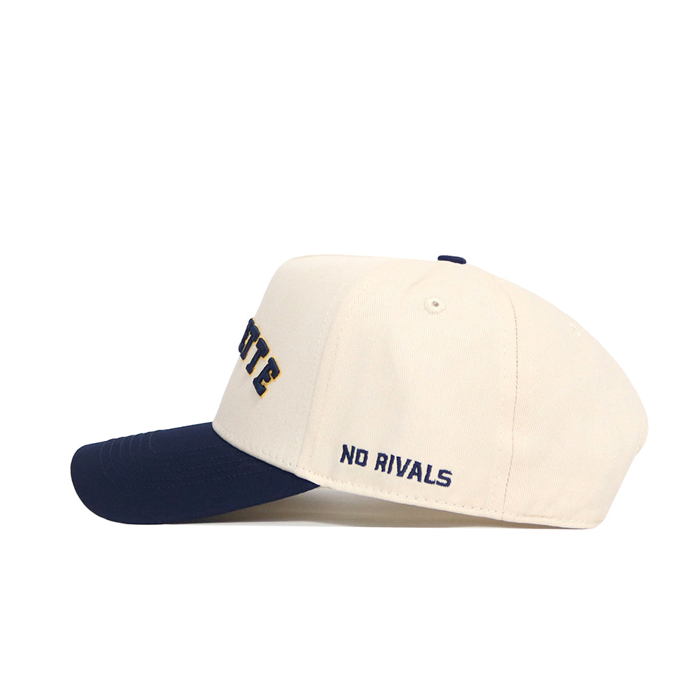 The Right Side Up MARQUETTE Hat by No Rivals features a cream cotton-canvas build, navy brim, "NO RIVALS" embroidered on the side, bold navy lettering on the front, and a snapback closure for a structured fit.