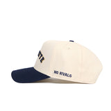 The Right Side Up MARQUETTE Hat by No Rivals features a cream cotton-canvas build, navy brim, "NO RIVALS" embroidered on the side, bold navy lettering on the front, and a snapback closure for a structured fit.
