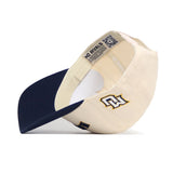 The Right Side Up MARQUETTE Hat by No Rivals, in classic cream and navy, is shown flipped upside down. The cotton-canvas snapback features an embroidered CW logo and “NO RIVALS” text on the inner band for a comfortable, structured fit.
