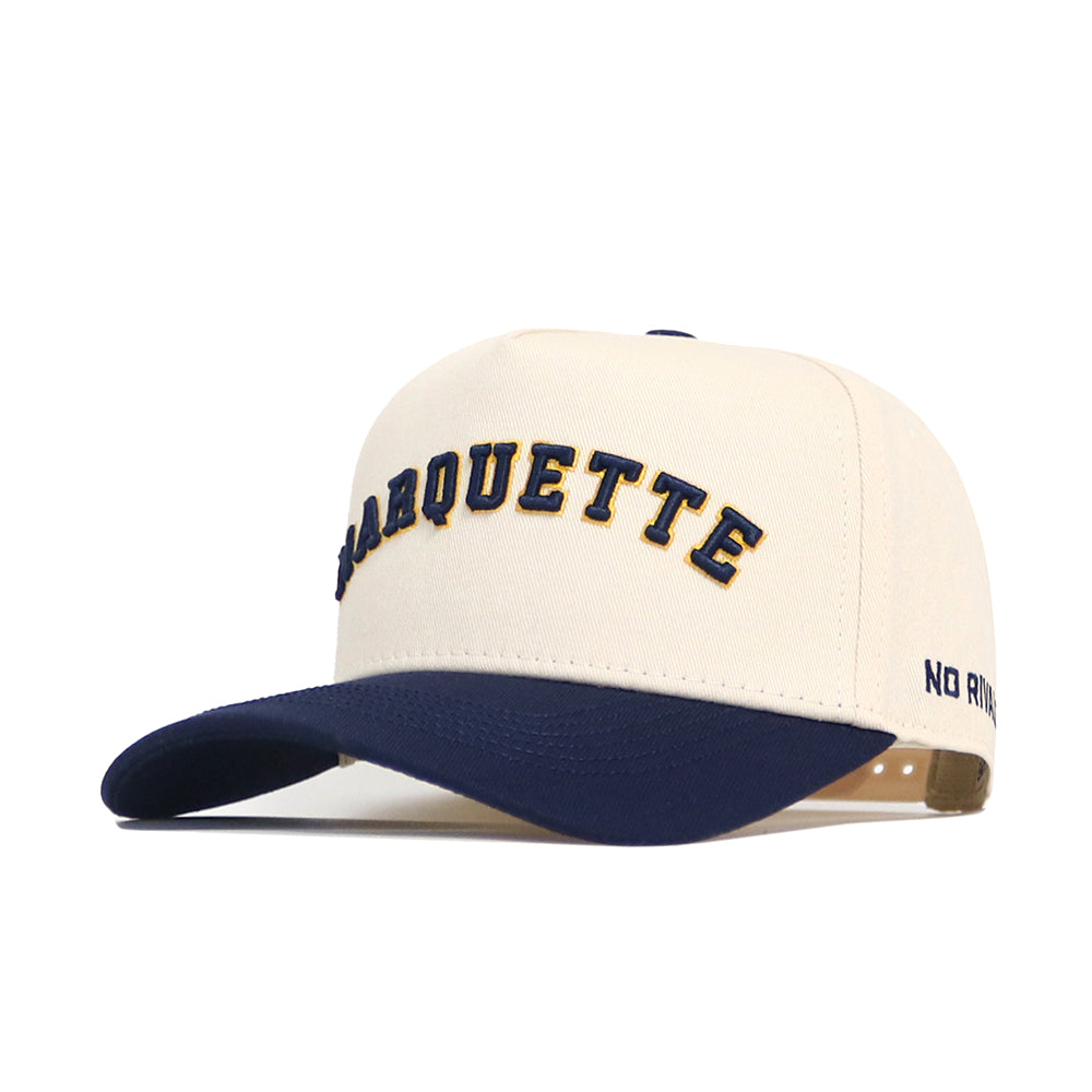 The No Rivals Right Side Up MARQUETTE Hat - Classic Colors is a cream cotton-canvas snapback with "MARQUETTE" in navy and gold on the front, a navy bill, and "NO REST" stitched on the left side.