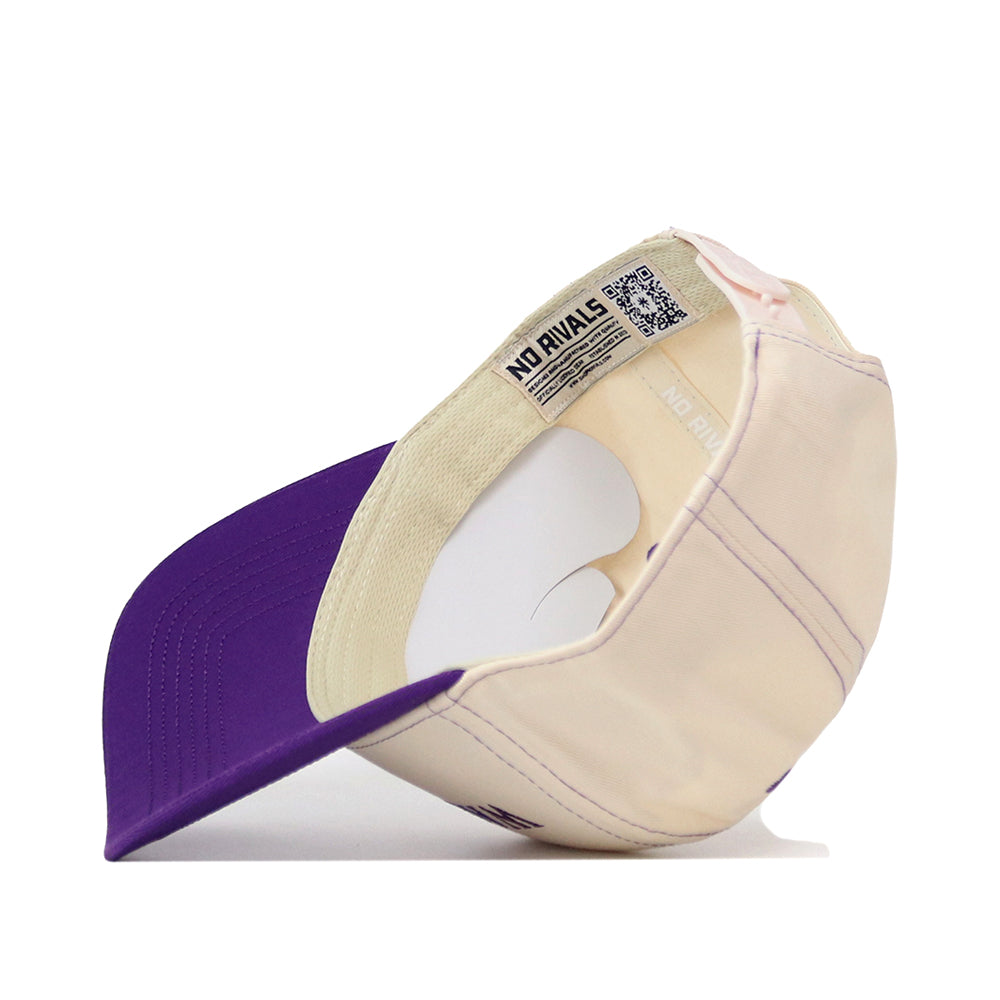 A Washington Huskies Vintage Hat by No Rivals is pictured upside down, revealing an inside label marked “NO RIVALS” alongside a QR code. The brim of the cap is purple, while the inner band has a light tone. This snapback cap offers an adjustable fit for personalized comfort and is crafted from high-quality cotton for lasting durability.