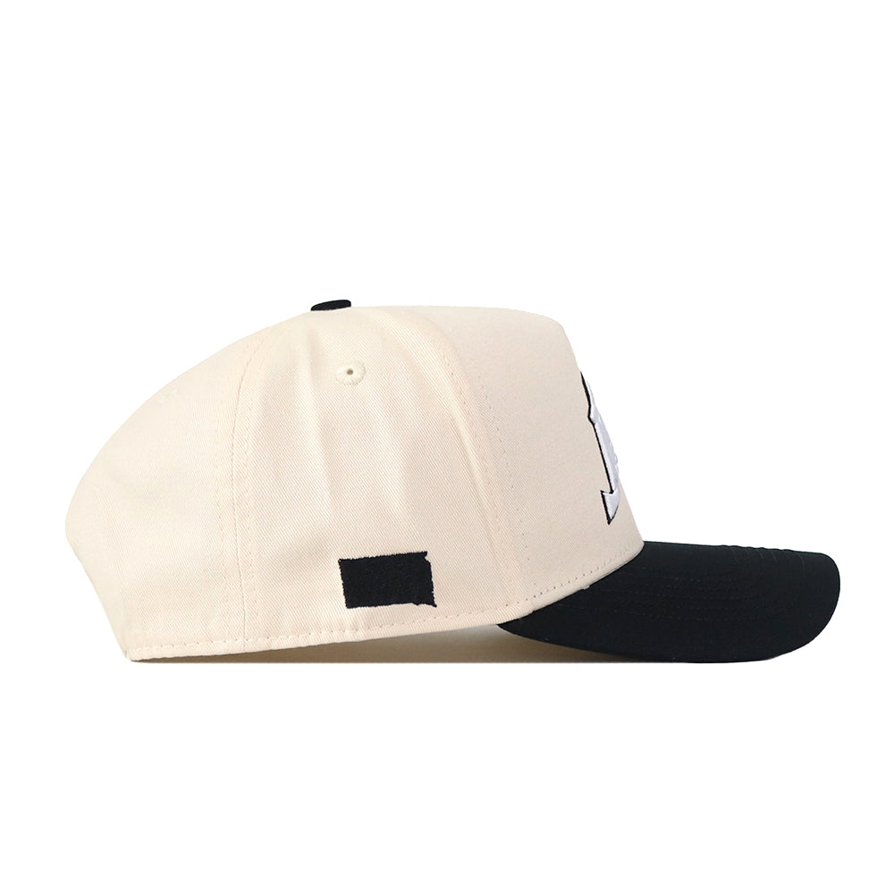 The South Dakota State Espresso Hat by No Rivals is a cream-colored baseball cap with a black brim, displayed from the side. Featuring a small black rectangular patch on the side and an embroidered logo, this cap adds a polished finish to any gameday ensemble.