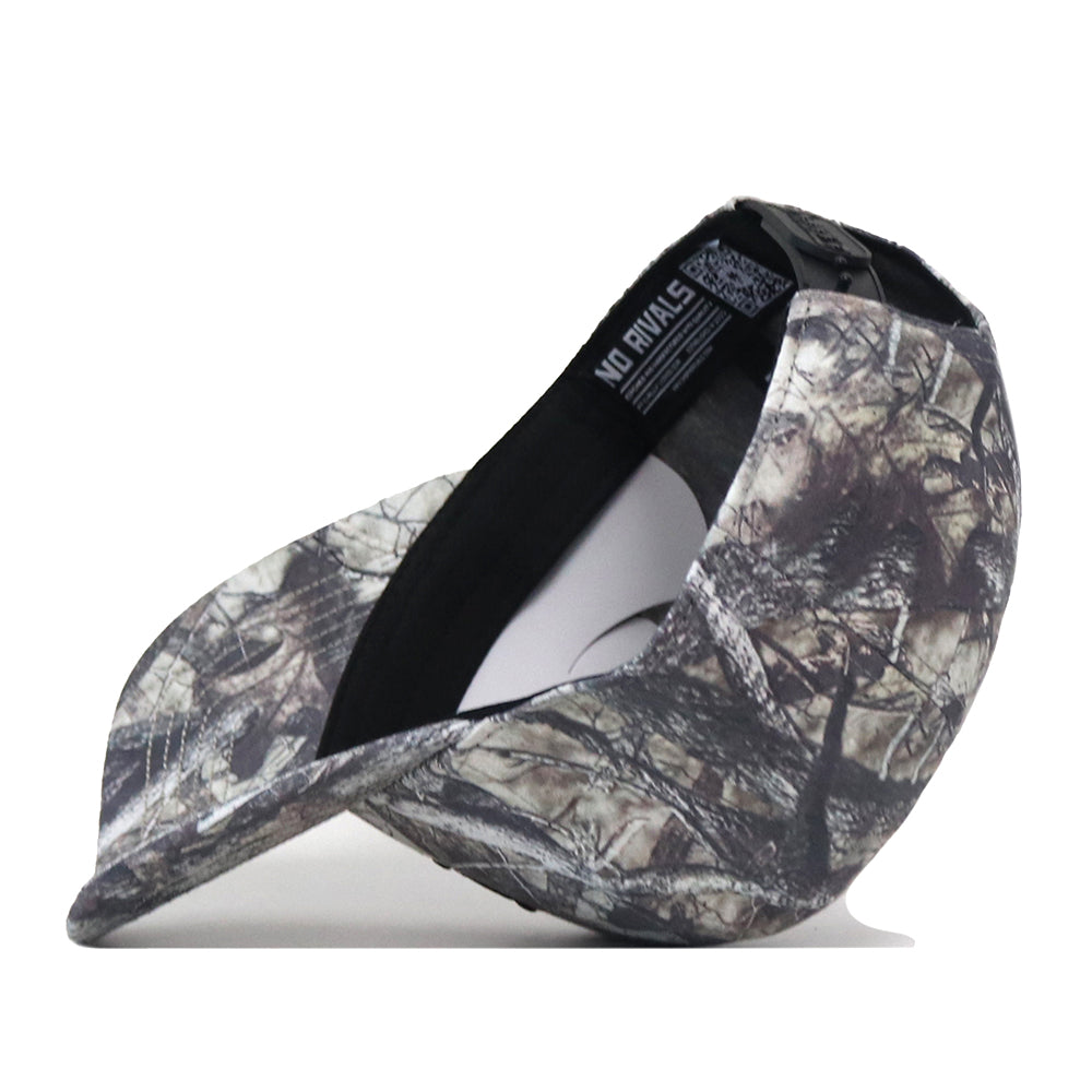 The Auburn Outland Hat by No Rivals is pictured from the side, featuring a camouflage design with a curved brim and the interior label displaying the No Rivals name. An officially licensed embroidered Auburn logo adds distinctive detail, while an adjustable snap back closure ensures a comfortable fit. The hat is shown against a plain white background.