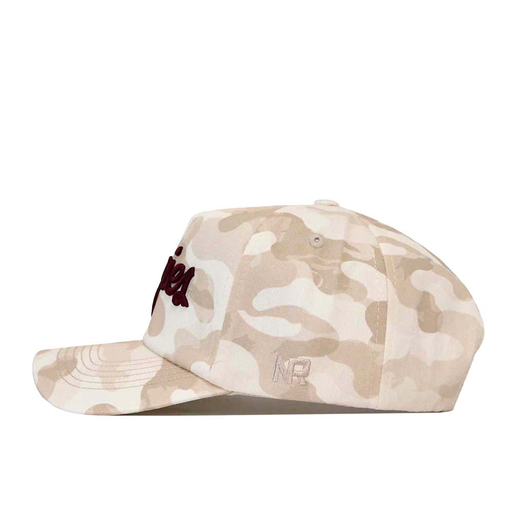 The No Rivals Texas A&M Script Sand Camo Hat – Unstructured is showcased from the side, featuring a beige and white camouflage pattern. Crafted from soft cotton fabric, this stylish snapback hat has a curved brim and embroidered logos on both the front and side, combining comfort with contemporary design.