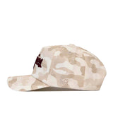 The No Rivals Texas A&M Script Sand Camo Hat – Unstructured is showcased from the side, featuring a beige and white camouflage pattern. Crafted from soft cotton fabric, this stylish snapback hat has a curved brim and embroidered logos on both the front and side, combining comfort with contemporary design.