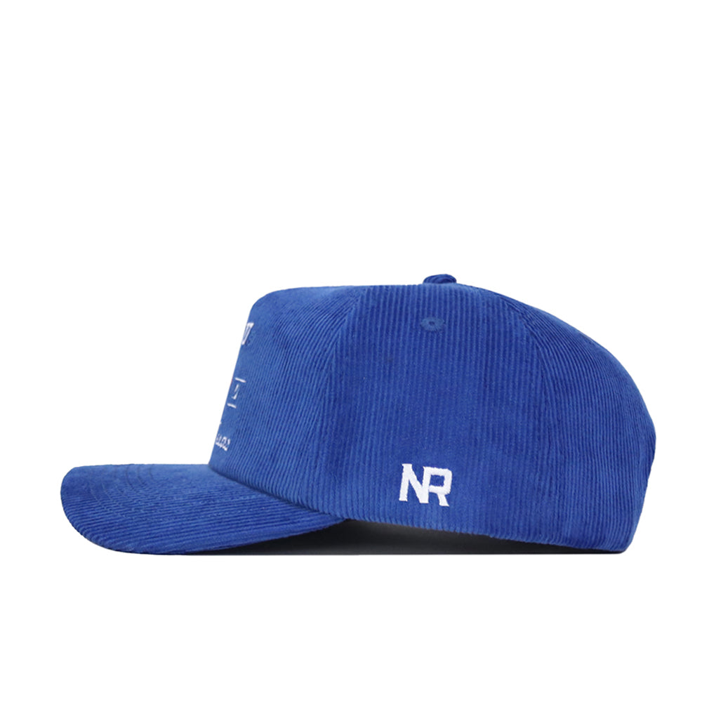 The SMU Vintage Cord Hat is a blue corduroy cap with a flat brim, snapback closure, and button on top. White "NR" embroidery appears on the back panel. The hat is adjustable and shown from the side.