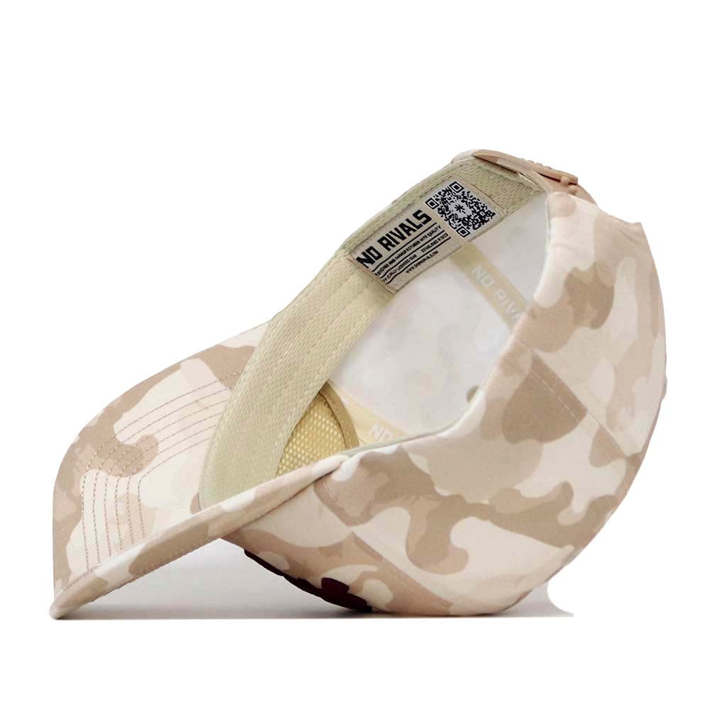 A Texas A&M Script Sand Camo Hat by No Rivals is displayed from the back, featuring a beige and cream camo pattern, made of durable cotton fabric with an adjustable strap. The inner label shows the No Rivals branding along with a visible QR code.