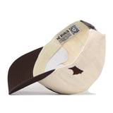 The Minnesota State University Mankato Espresso Hat by No Rivals is a cream and brown snapback, flipped upside down to display its inside tag featuring the NO RIVALS logo and a small Minnesota state-shaped patch on the side—the ideal finishing touch for your next gameday outfit.