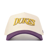 The No Rivals JMU Vintage Wordmark Hat (B2B) features a cream color, "DUKES" embroidered in yellow with a purple outline on the front, a purple curved brim, an unstructured fit, and an adjustable snapback for most sizes.