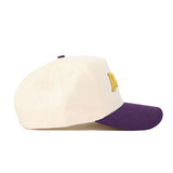 The No Rivals JMU Vintage Wordmark Hat (B2B) is a cream baseball cap with a purple brim, yellow embroidered front letters, unstructured fit for comfort, and snapback adjustment. Shown from the side.