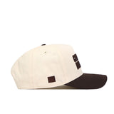 A side view of the No Rivals Colorado Buffaloes Espresso Hat, a cream-colored snapback baseball cap with a black brim. It features a small black square patch on the side and raised black text partially visible on the front, including an officially licensed embroidered Colorado Buffaloes logo.