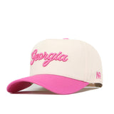 Introducing the Georgia Pink Out Hat by No Rivals—a beige snapback featuring “Georgia” embroidered in pink script on the front and a pink curved brim. The side showcases the No Rivals initials (NR) stitched in pink, making it a stylish way to support the National Breast Cancer Foundation.
