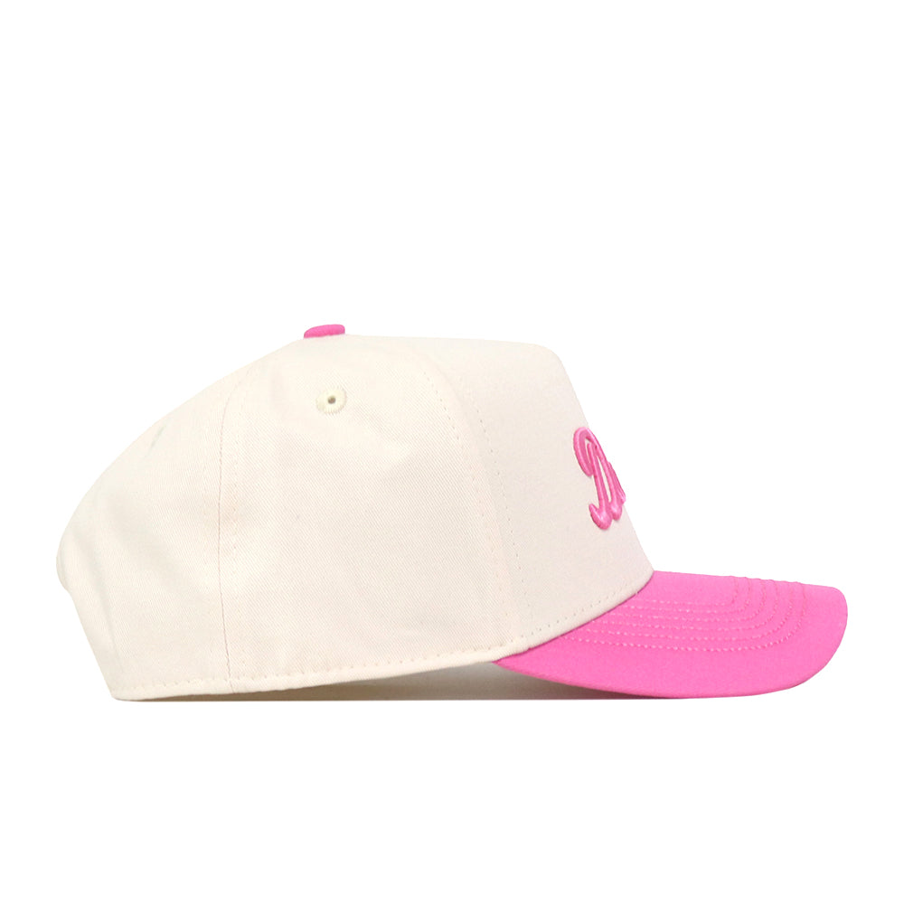 A side view of the Dallas Pink Out Hat by No Rivals, featuring a white crown, pink brim, and pink embroidered text on the front, shown against a white background. This officially licensed breast cancer awareness cap includes a convenient snapback adjustment for a comfortable fit.