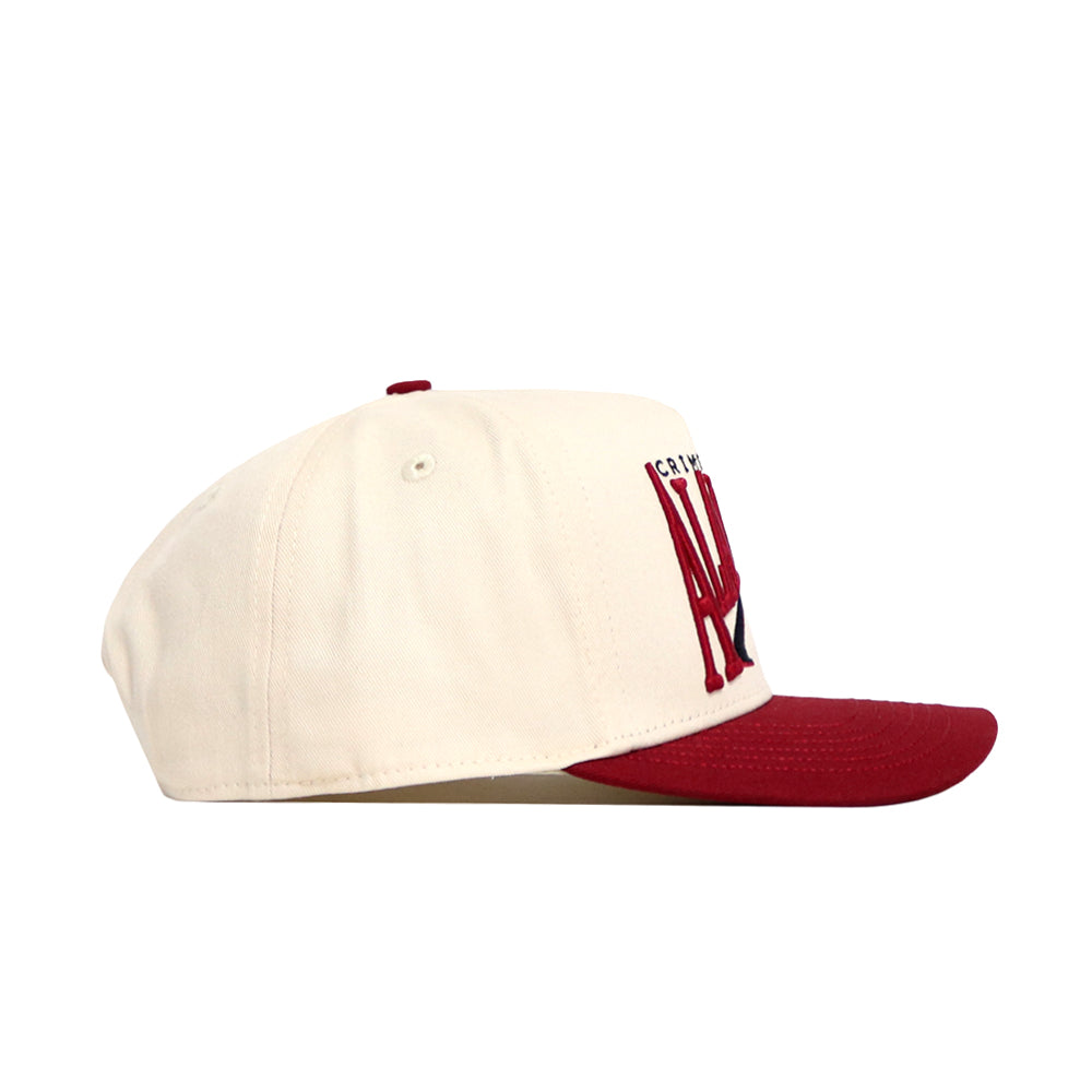 The Alabama Stride Hat by No Rivals is a cream snapback with a flat maroon brim and maroon embroidered letters, crafted from high-quality cotton. Shown in side profile against a white background.