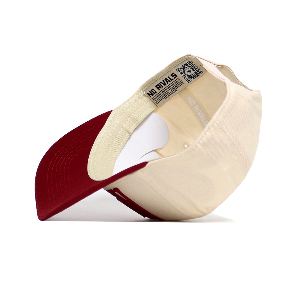 The Alabama Stride Hat by No Rivals is a beige and red cotton baseball cap with a structured fit, curved dark red bill, and an inner label reading NO RIVALS plus a QR code on the band. The photo shows it flipped to display these details.