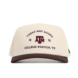 The No Rivals Texas A&M Outlaw Hat - Classic is a white snapback baseball cap with a structured fit, brown brim, and “Texas A&M Aggies 1876 College Station, TX” embroidered on the front. Made from high-quality cotton for comfort and durability.
