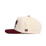 The No Rivals Texas A&M Stride Hat is a cream baseball cap with a maroon brim, front embroidered text, side NR logo in maroon, ventilation eyelets, top maroon button, and snapback closure. Made from high quality cotton.