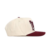 The No Rivals Texas A&M Stride Hat features a cream snapback design in premium cotton, with a maroon brim and maroon embroidered lettering and design on the front, shown from the side.