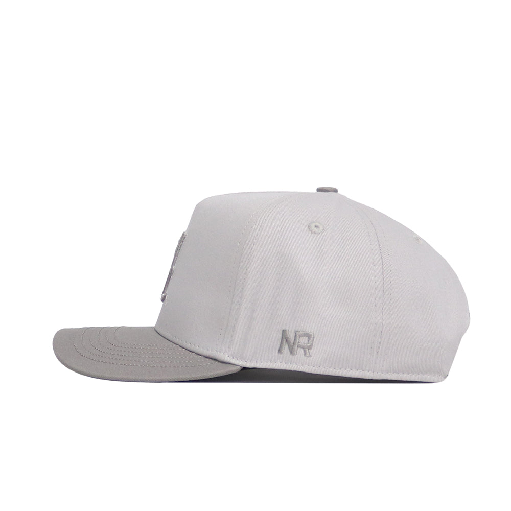 The Alabama Graphite Hat by No Rivals is a light gray structured hat with a flat brim, embroidered NR graphics on the back side panel, and a classic snapback closure, shown from the side.