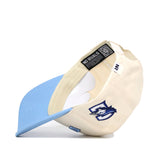 The Upside Down CREIGHTON Hat - Light Blue by No Rivals is a cream cotton-canvas snapback with a light blue brim, wolf logo on the side, and blue patch on the back. Shown upside down to reveal interior tags and stitching.