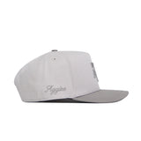 The No Rivals Texas A&M Graphite Hat is a structured, light gray snapback with a slightly darker flat brim. Made from premium cotton, it features "Aggies" script embroidery on the left side and is shown in profile, facing right.