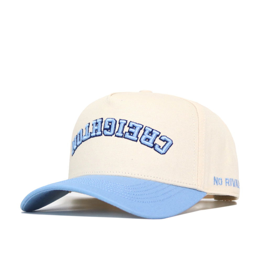 The Upside Down CREIGHTON Hat - Light Blue by No Rivals is a cream cap with a light blue brim, high-quality cotton, structured fit, blue "CREIGH" embroidery up front, "NO RIVAL" on the side, and a snapback closure.