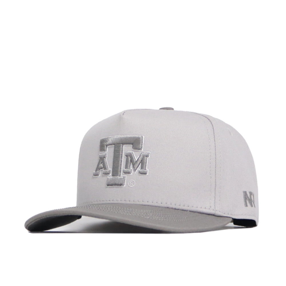 The Texas A&M Graphite Hat by No Rivals is a light gray snapback with a flat brim, featuring the embroidered ATM logo on the front and NFL logo on the side, made from high-quality cotton for a structured fit.