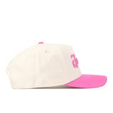 A cream-colored Michigan State Pink Out Hat by No Rivals, officially licensed and featuring a pink brim with pink embroidered lettering on the front, is shown from the side against a white background. This stylish snapback not only offers comfort but also serves as a breast cancer awareness hat, supporting an important cause.